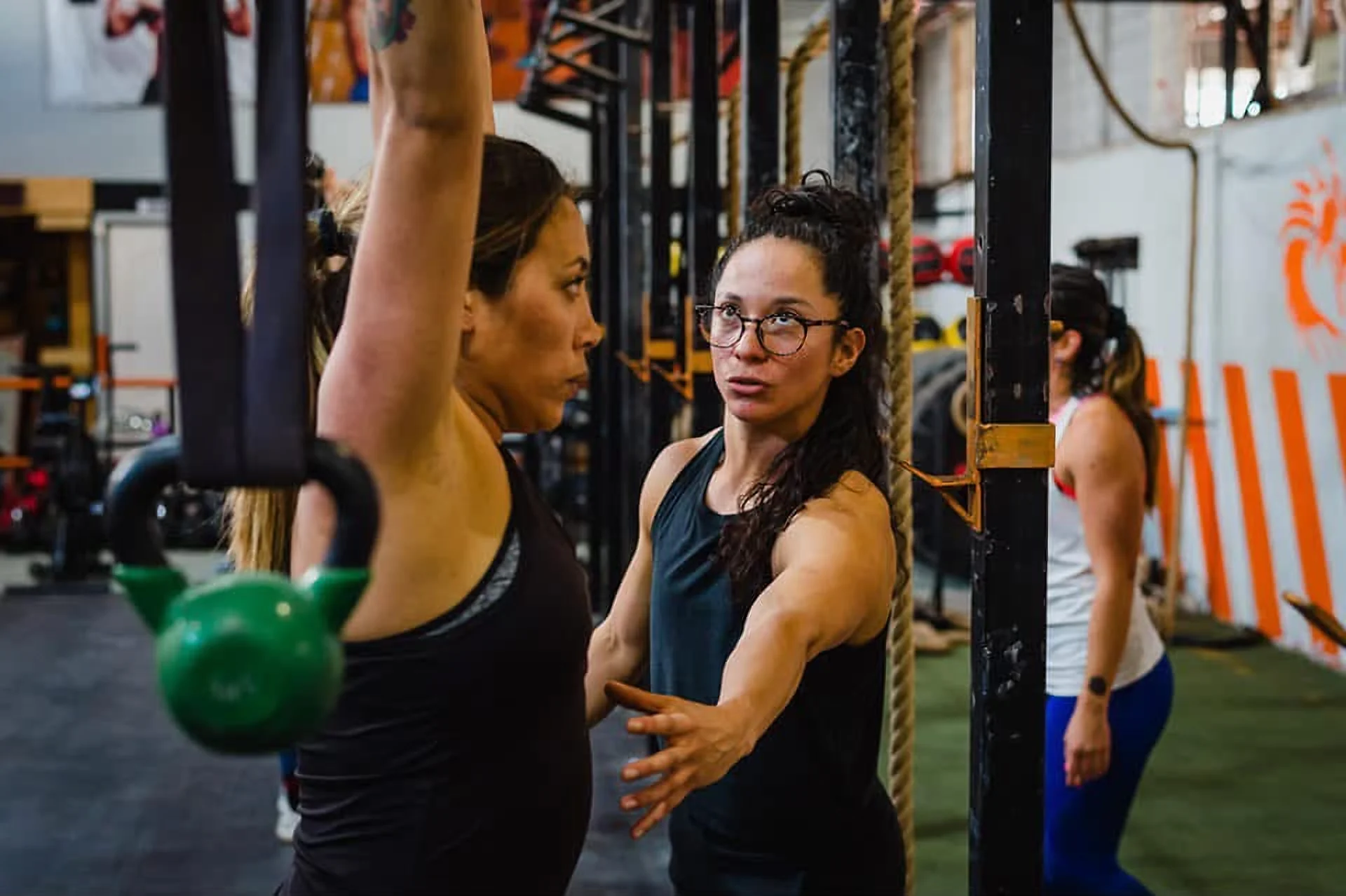 Niria corrige a una atleta que sostiene una kettlebell sobre la cabeza